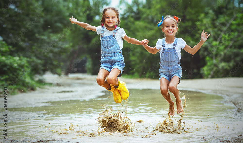 快乐有趣的姐妹双胞胎小女孩穿着橡胶靴在水坑上跳