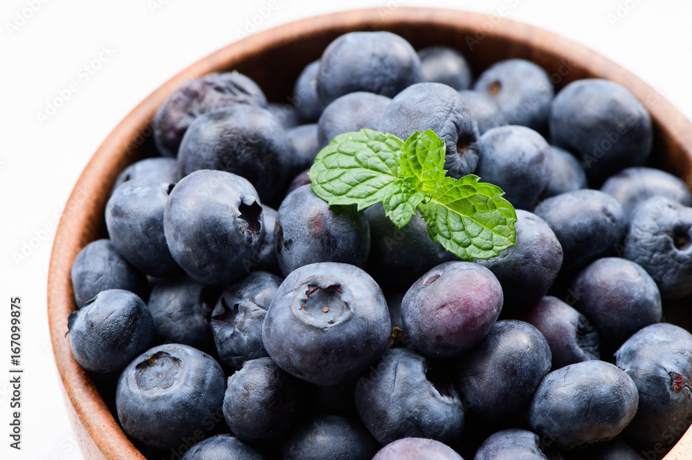 将蓝莓和香草薄荷放在一个木碗中，在白色背景上隔离