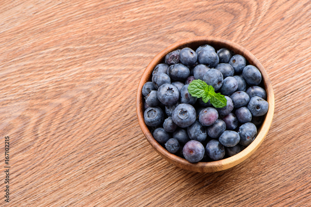 木制背景木碗中的蓝莓和香草薄荷，俯视图