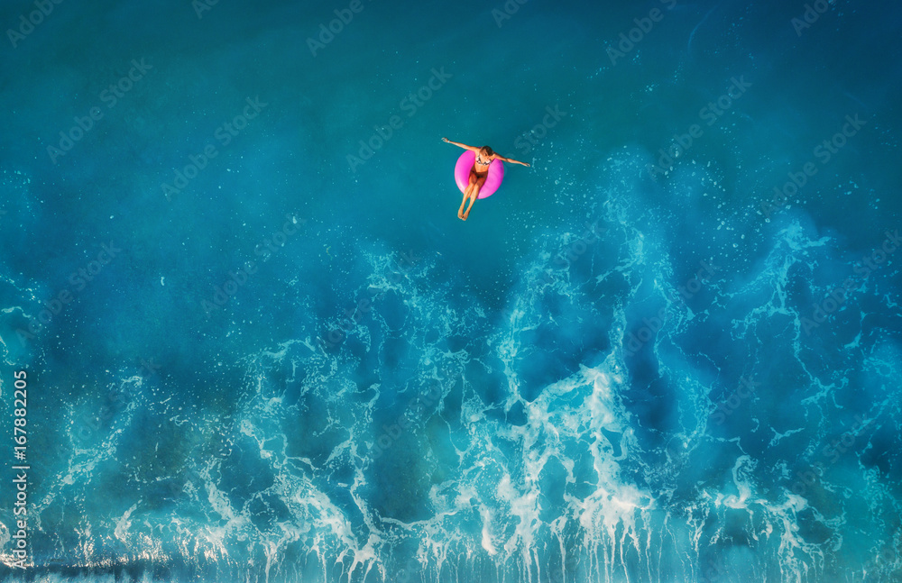 Aerial view of young woman swimming on the pink swim ring in the transparent turquoise sea in Oluden