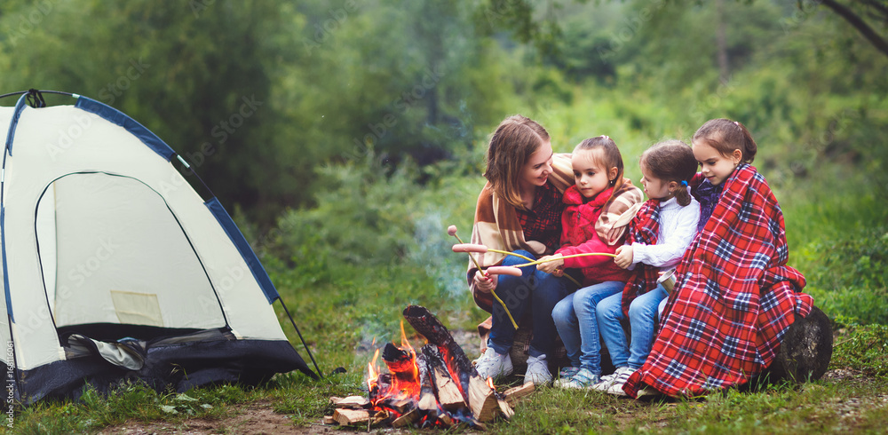 快乐的旅游家庭徒步旅行。母亲和孩子在帐篷附近的篝火上炸香肠
