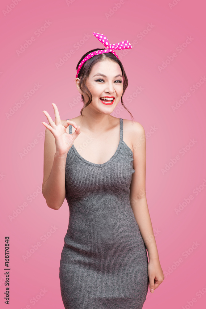 粉色背景下，一个亚洲女孩的肖像，她带着漂亮的微笑，粉色背景上有手势