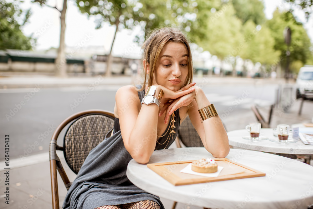 年轻漂亮的女人坐在户外的法式咖啡馆里看着甜蛋糕