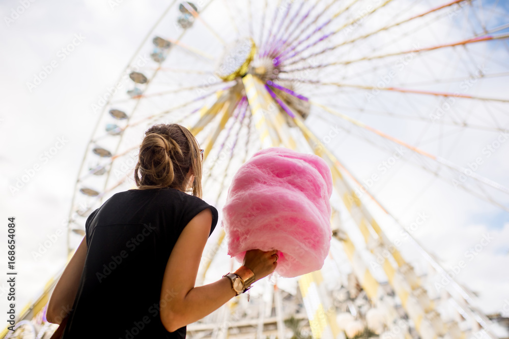 年轻女子拿着粉色棉花糖站在游乐园的摩天轮前