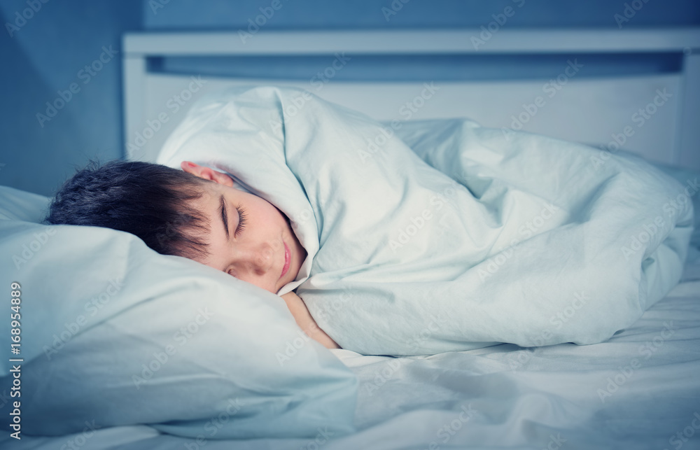 男孩穿着睡衣睡在床上。孩子晚上躺在床上的枕头上