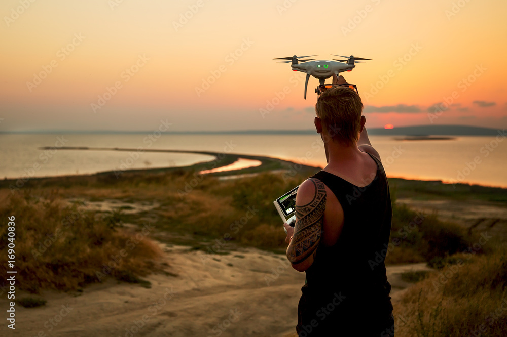 日落时，无人机在海上飞行。男子从空中降落无人机。日落照片从空中拍摄