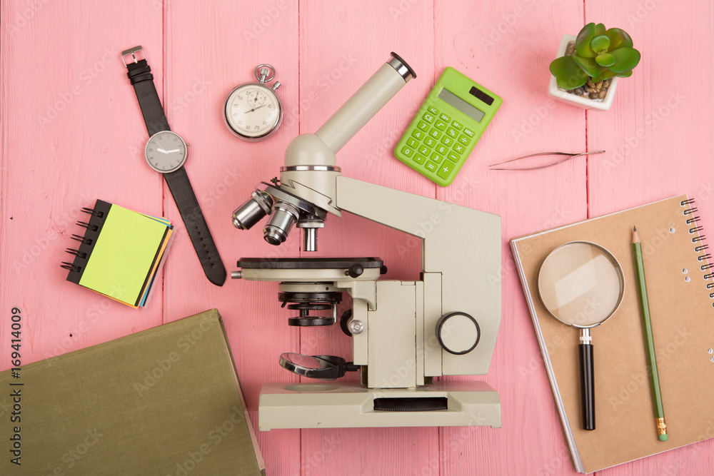 Education concept - notepad, microscope on the pink wooden desk