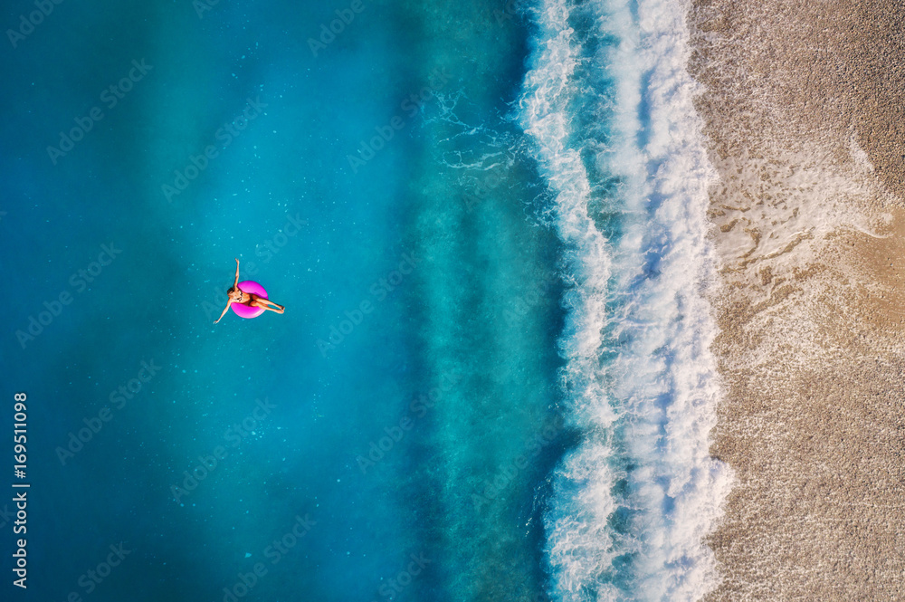 奥卢登透明绿松石海中，一名年轻女子在粉色游泳圈上游泳的鸟瞰图