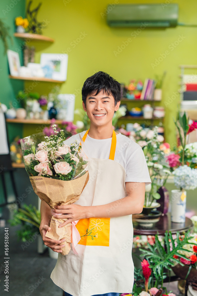 英俊的男花商站在花店里，手里拿着一束花