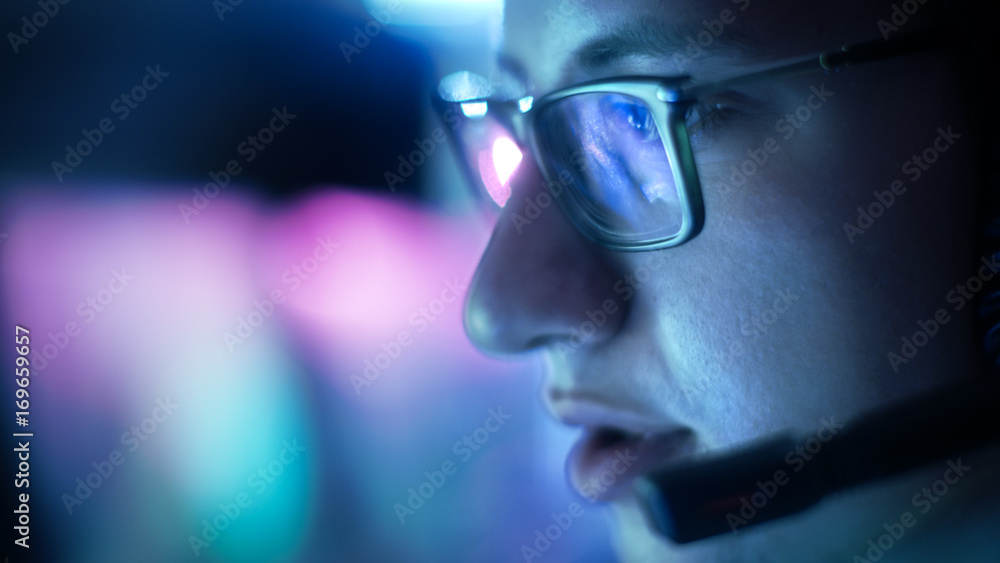 戴眼镜的青少年戴着耳机玩电子游戏向麦克风发出命令的特写