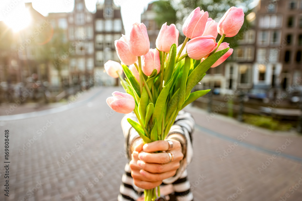 站在阿姆斯特丹市户外，一位女士献上一束美丽的粉色郁金香