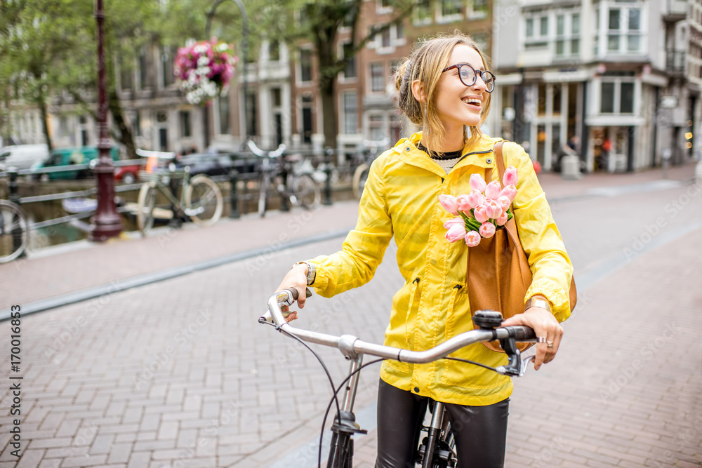 阿姆斯特丹市一名身穿黄色雨衣、挎包带花的年轻女子骑自行车