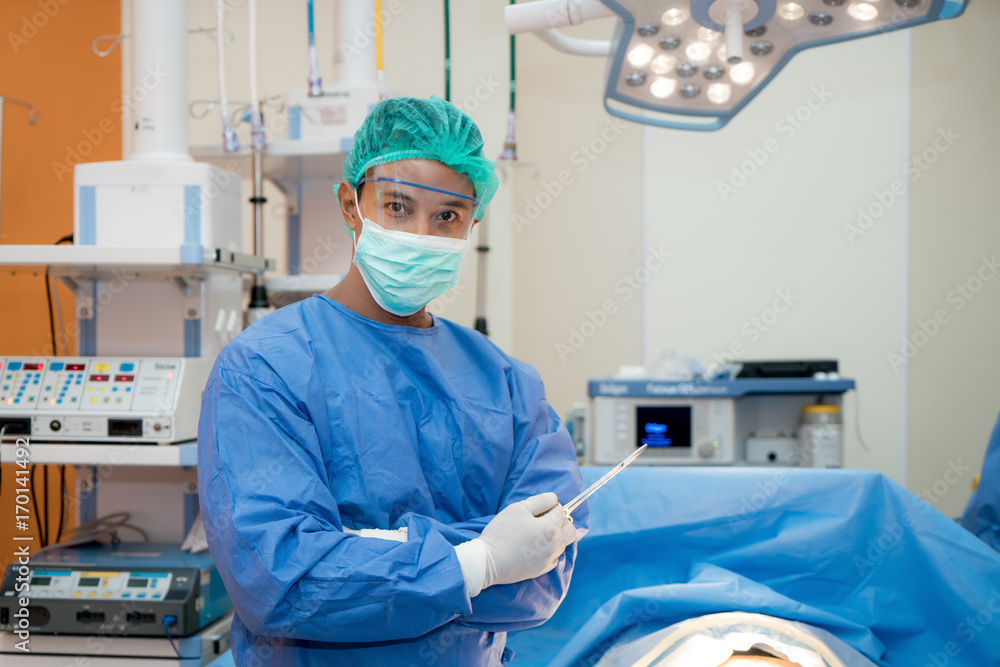 亚洲微笑外科医生手持手术剪刀，双臂交叉，站在su中