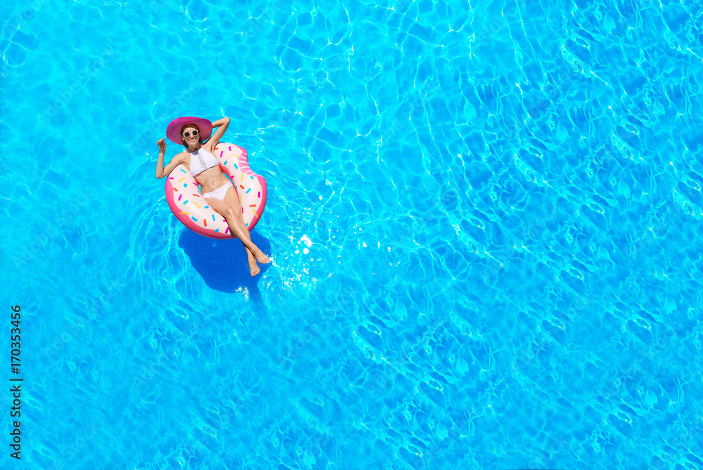 蓝色游泳池里带充气甜甜圈的漂亮年轻女子