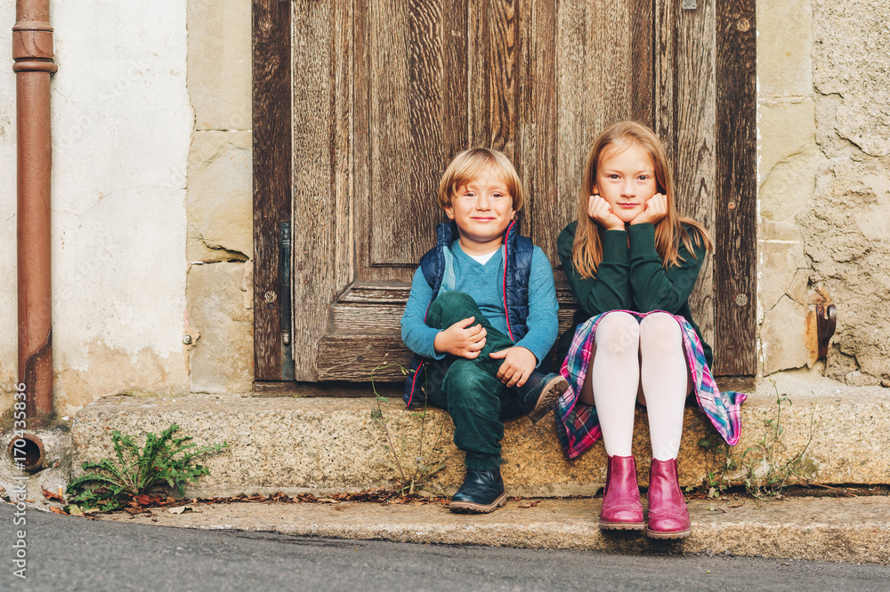 两个时尚的孩子在户外摆姿势，在老式门旁休息。时尚适合学生。