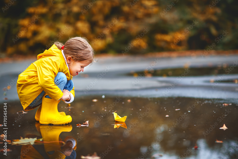 快乐的小女孩，带着纸船在秋天的水坑里享受大自然。