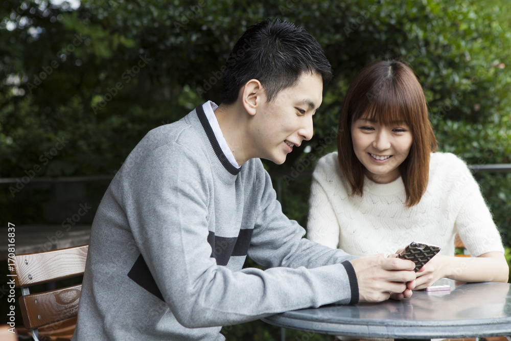 年轻夫妇在咖啡馆露台上看智能手机
