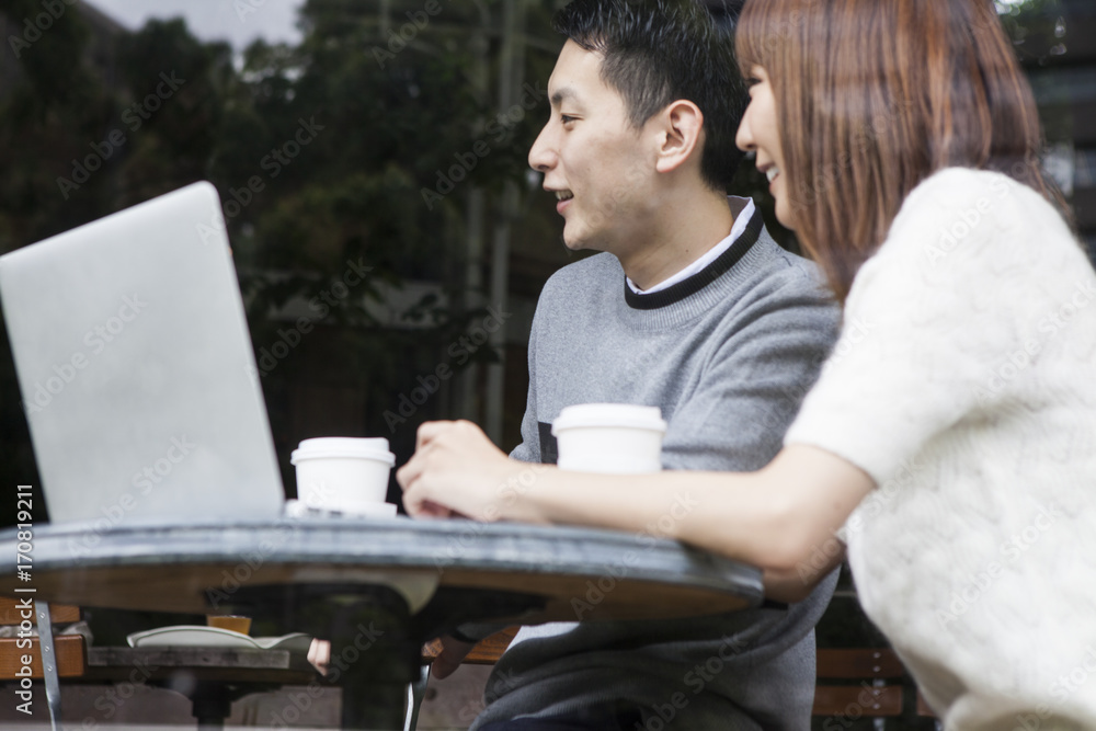 一对年轻夫妇在咖啡馆露台上看笔记本电脑时聊天
