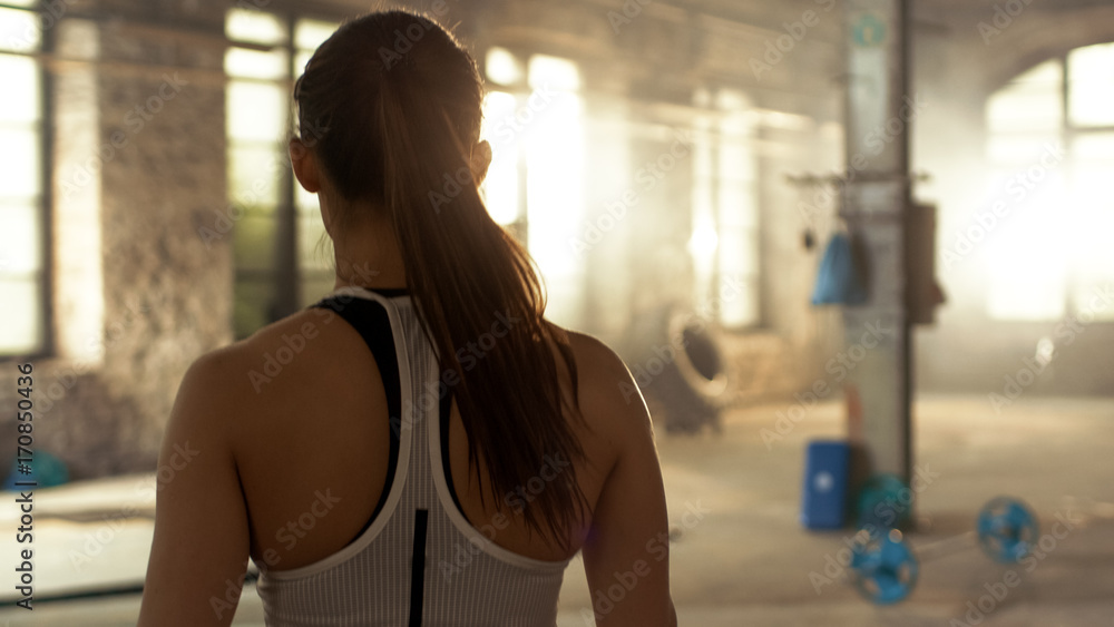 从运动美女进入健身房的背后拍摄。她很自信，建筑是工业的