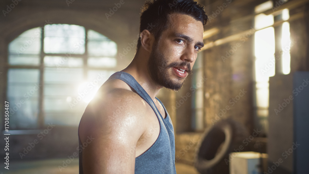 精疲力竭的肌肉男在健身房锻炼后看着镜头。汗水从他身上滴下来