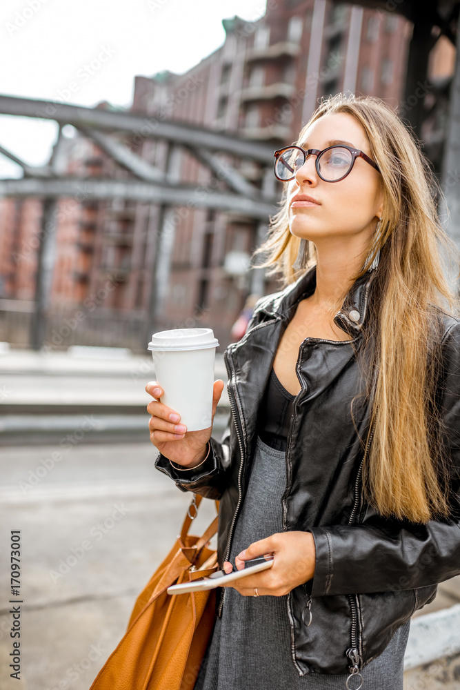 一位穿着皮夹克、戴着咖啡杯在户外行走的时尚女商人的生活方式画像