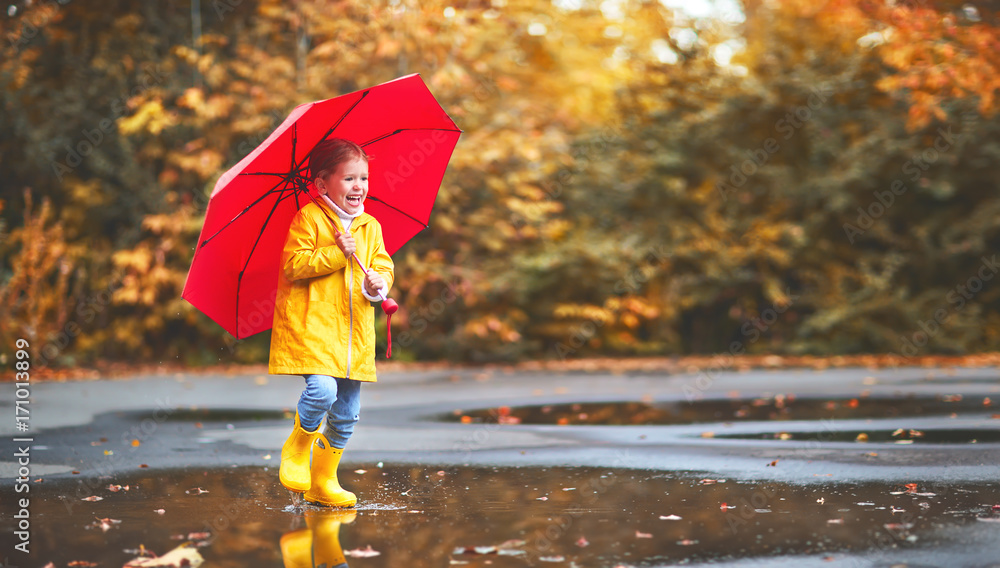 快乐的小女孩，带着雨伞和橡胶靴在水坑里秋天散步