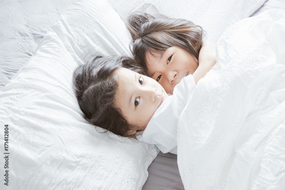 两个亚洲中国小女孩拥抱在一起，躺在床上。