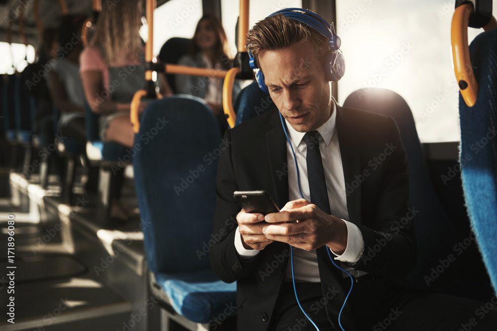 戴着耳机在公交车上读短信的年轻商人