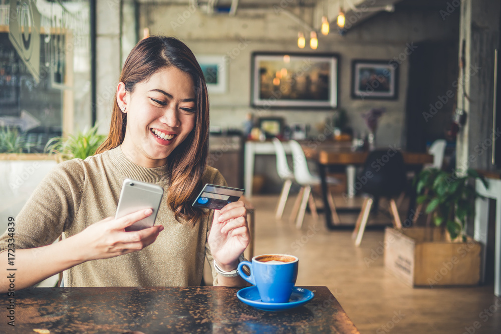 年轻漂亮的亚洲女人在咖啡馆用智能手机和信用卡在线购物