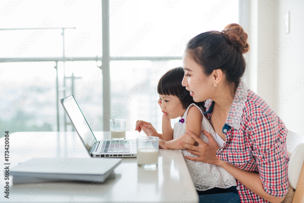 亚洲女妈妈带着女儿在电脑前工作
