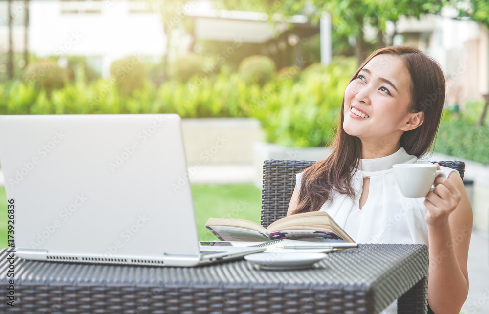 年轻漂亮的亚洲女人在户外公园用笔记本电脑/互联网/网上购物，微笑/新鲜