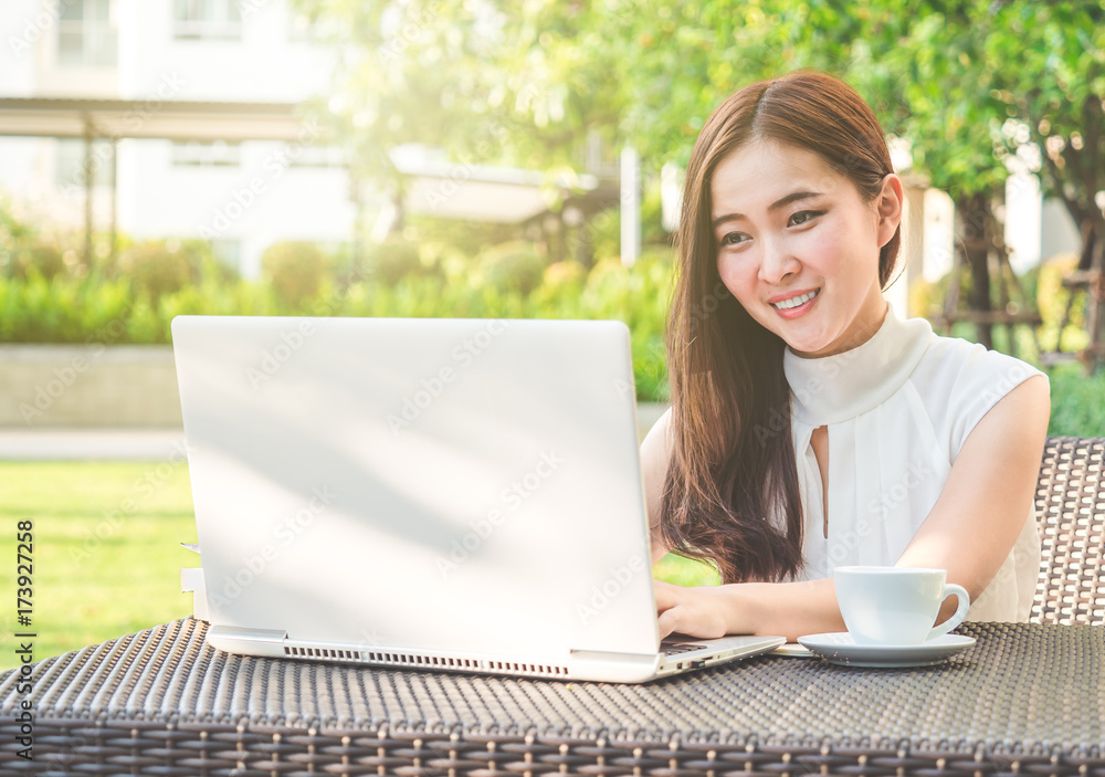 年轻漂亮的亚洲女人在户外公园用笔记本电脑/互联网/网上购物，微笑/新鲜