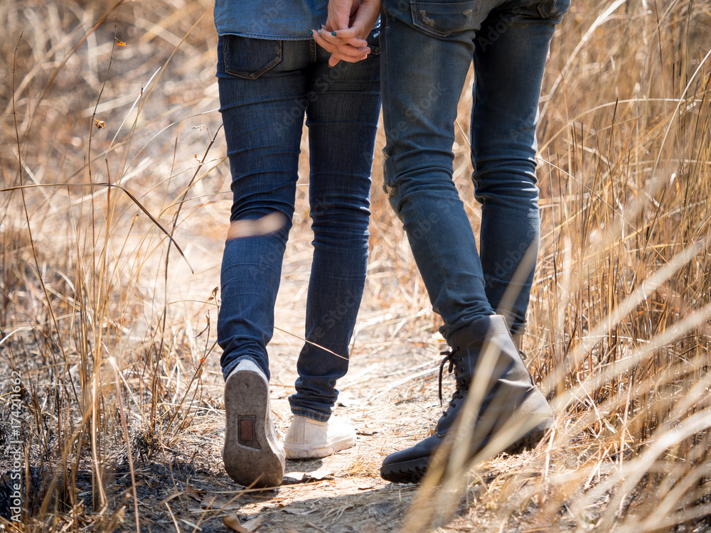 两对年轻夫妇穿着牛仔裤，手牵着手在草地上，看起来很时髦，步行去山里旅行