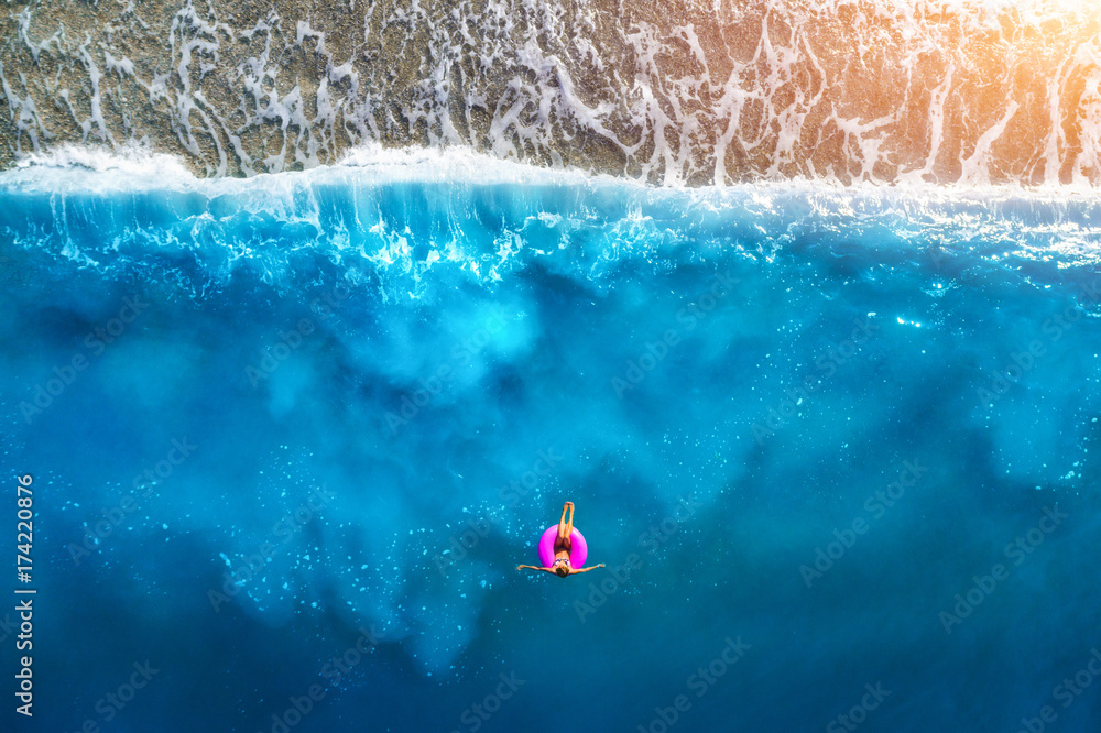 Oludeni透明绿松石海中，苗条女子在粉色游泳圈上游泳的鸟瞰图