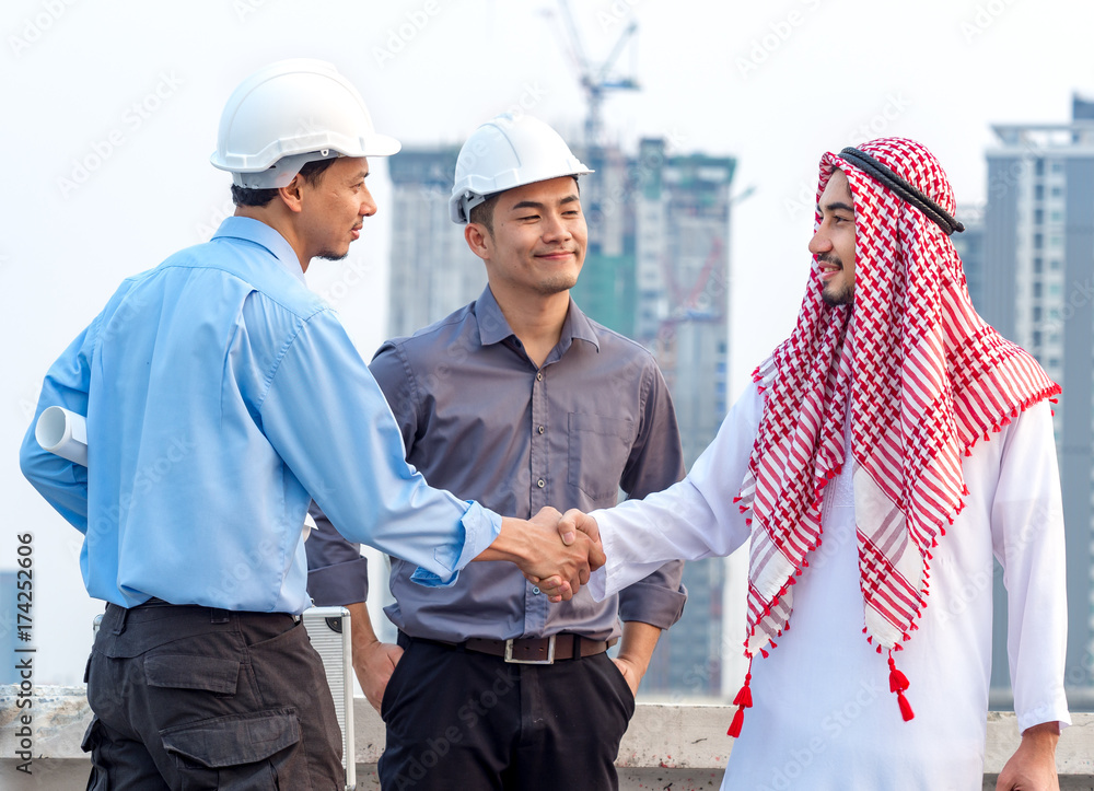 年轻的亚洲工程师/建筑师与阿拉伯商人握手，谈论项目