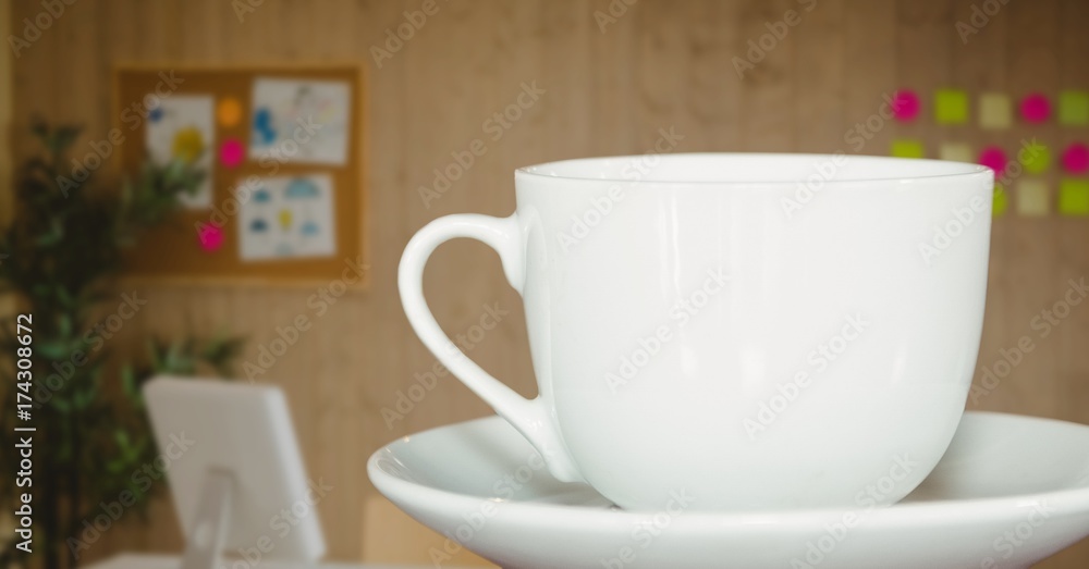 白色咖啡杯放在茶托上，对着昏暗的模糊办公室