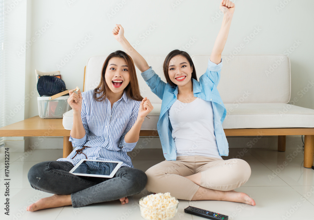 两个女朋友坐在沙发附近的地板上看电影，吃爆米花，一起放松