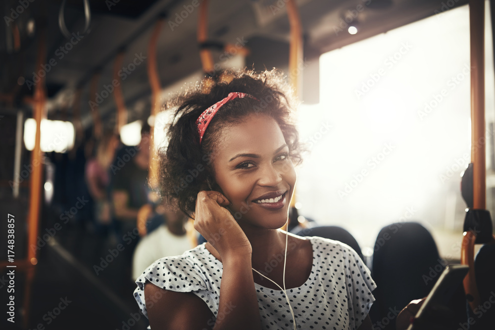 微笑的非洲女人站在公交车上听音乐