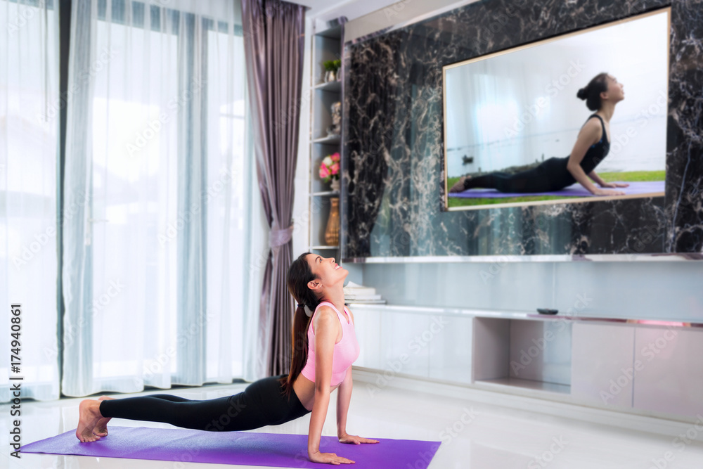 亚洲女士在电视上跟随教练开始训练瑜伽