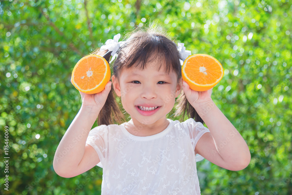 野餐间隙，一个亚洲小女孩拿着橘子在公园里微笑