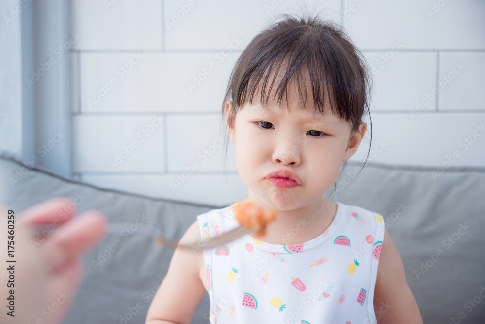 一个亚洲小女孩，脸上挂着不开心的表情，妈妈想让她吃午饭，挑食的孩子。