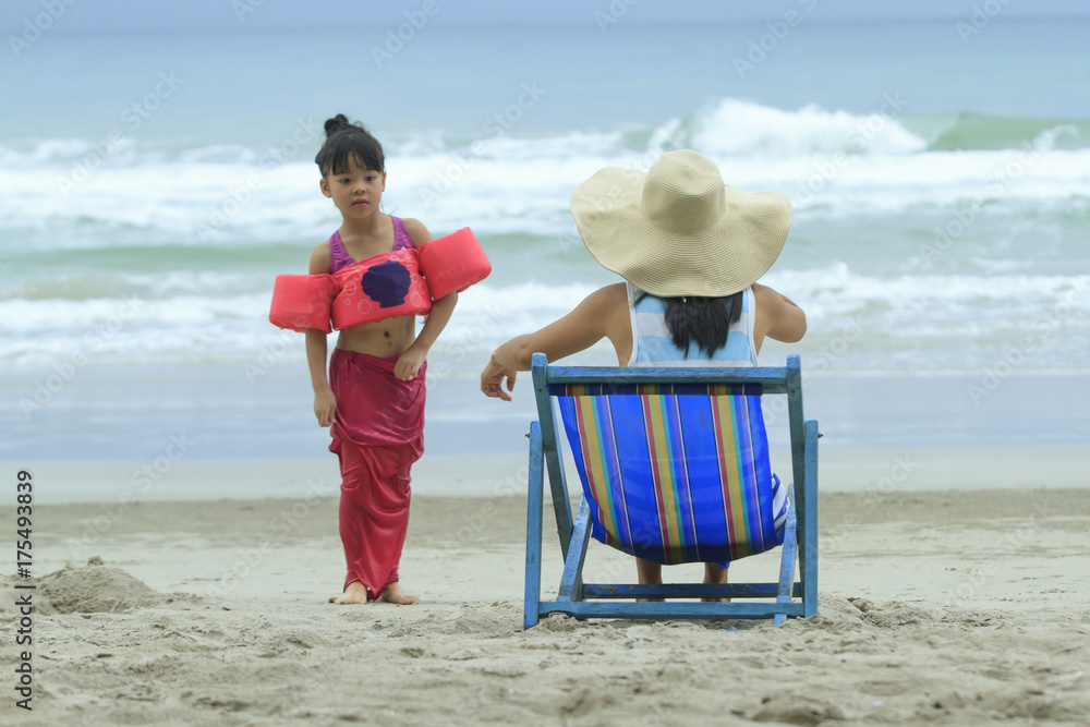 母亲坐在海滩的躺椅上，看着女儿玩耍，家庭生活方式旅行健康