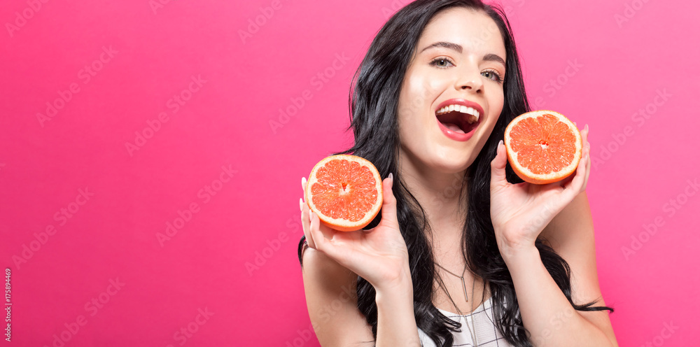 粉红色背景下拿着橘子的快乐年轻女人