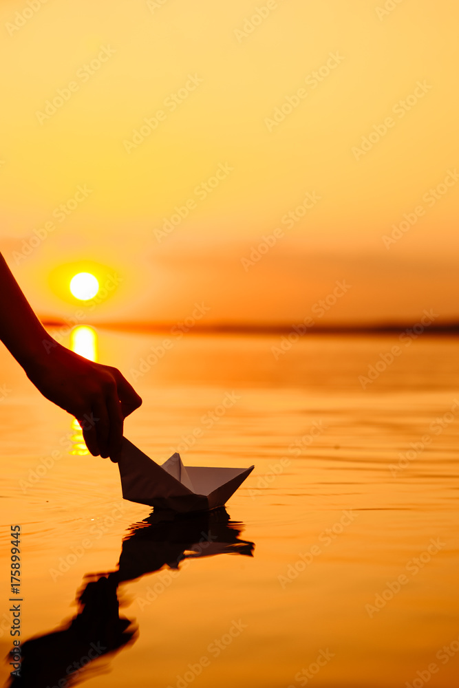 一个孩子把一艘纸船放进水里。美丽的日落。折纸。河流。湖泊。