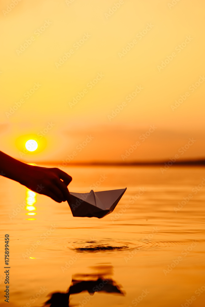 一个孩子把一艘纸船放进水里。美丽的日落。折纸。河流。湖泊。