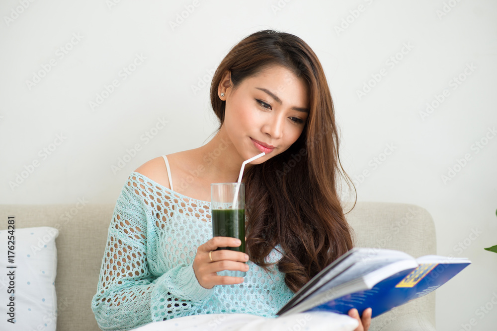 微笑的年轻亚洲女性在家喝绿色新鲜蔬菜汁或冰沙
