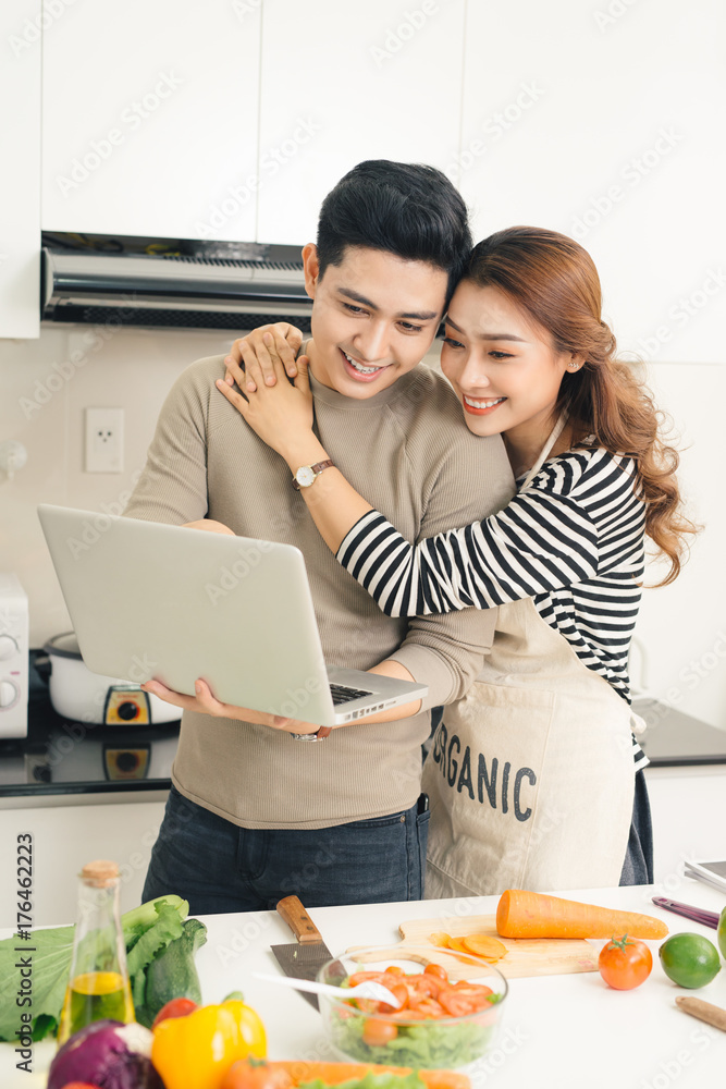 一名亚洲女子在厨房向男友展示笔记本电脑上的东西