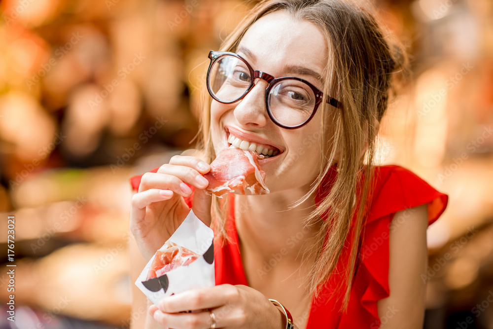 一位身穿红色连衣裙的年轻女子坐在餐厅吃着果酱传统的西班牙干腌火腿的画像