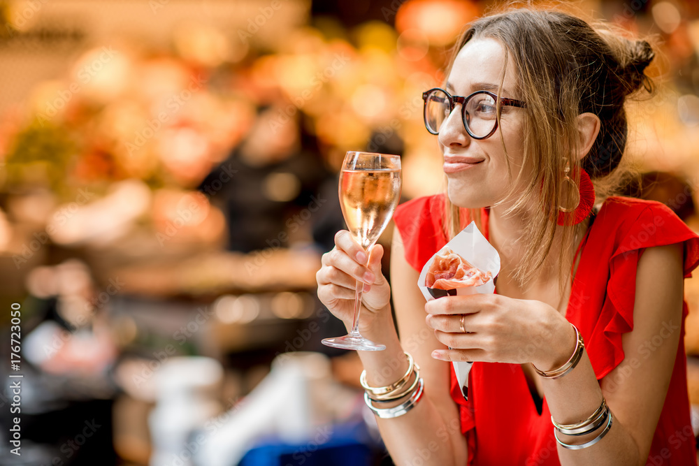 一位身穿红色连衣裙的年轻女子坐着吃着果酱传统的西班牙干腌火腿，配上一杯葡萄酒