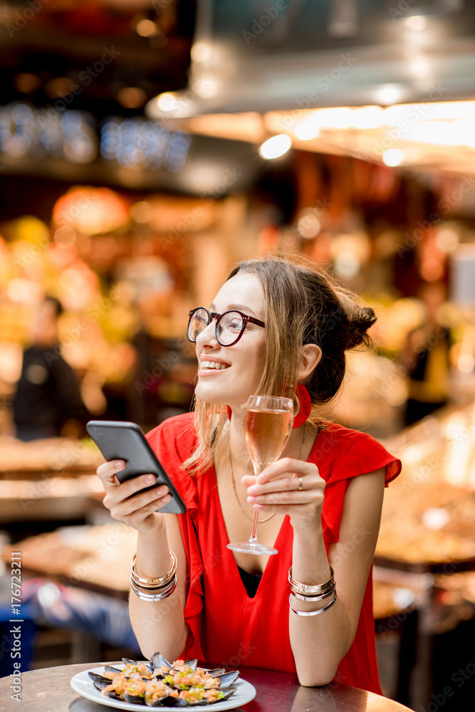 一位身穿红色连衣裙的年轻女子坐在食品市场上与贻贝和玫瑰酒共进午餐